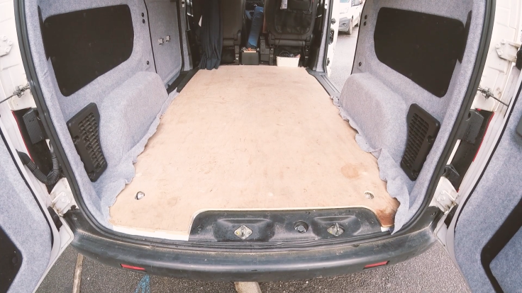 The dirty plywood van floor, looking in from the back doors