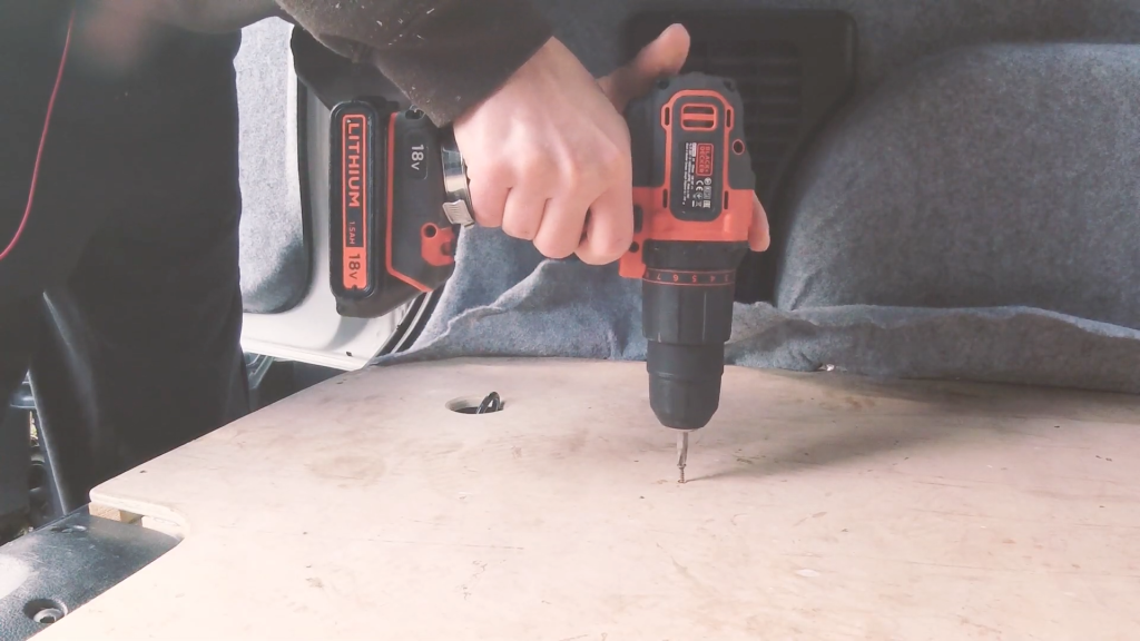 A drill unscrewing screws from the van floor