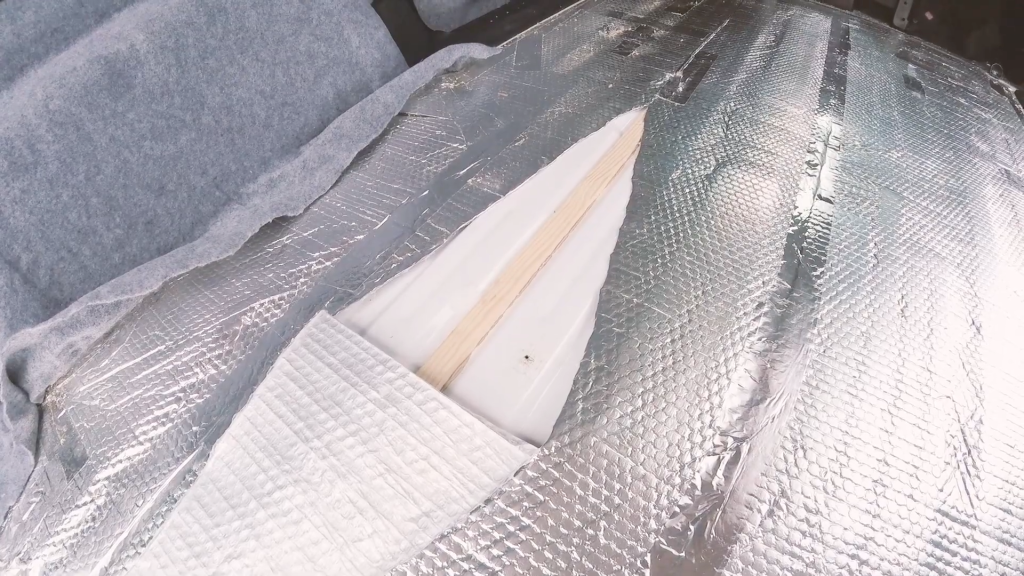A rip in the silver bubble wrap insulation on the floor, showing the metal and wood strip wood beneath